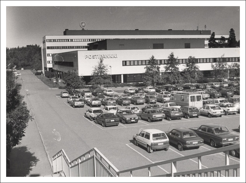 Vanha kuva Hervannan Postipankin maksupalvelukeskuksesta. Kuvassa rakennus ulkoa. Vanhoja autoja ja parkkipaikka.